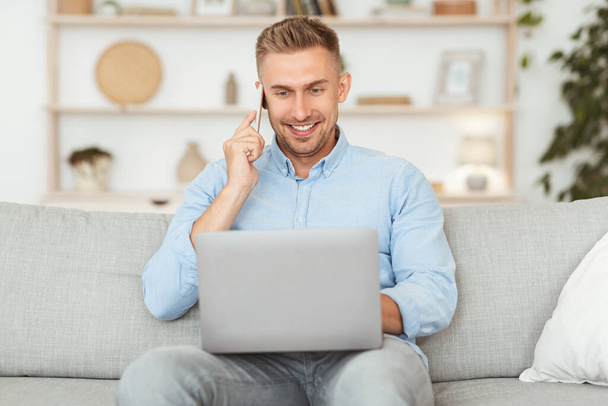 Portrait of successful smiling man talking on cellphone using pc - Photo, Image