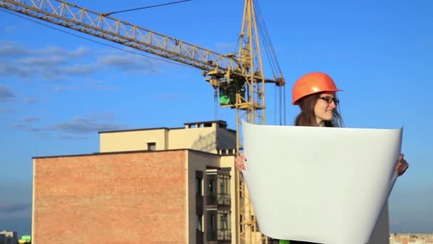 Νεαρή γυναίκα μηχανικός με σχέδιο στα χέρια επιθεωρεί την κατασκευή - Πλάνα, βίντεο