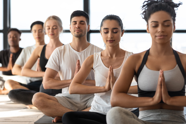 Harmonie mentale. Groupe de jeunes amateurs de yoga sportif méditant ensemble en studio - Photo, image
