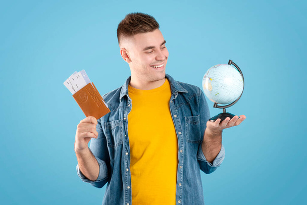 Handsome man with documents and globe ready for journey around world on blue studio background - Photo, image