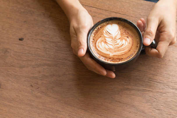 Frauenhand hält Piccolo-Latte-Kunst in einer Tasse, die schöne Herzkunst aus Milch belegt. - Foto, Bild