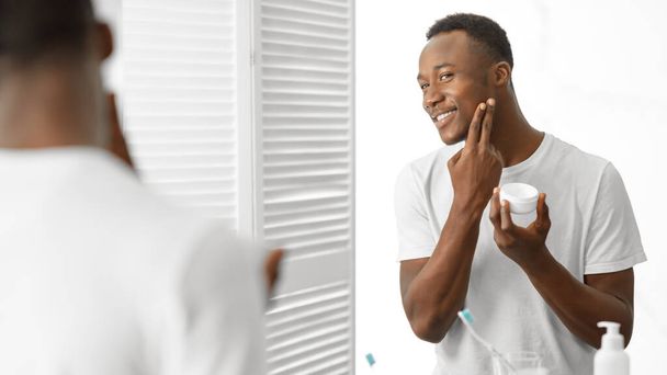 African Man Using Facial Cream Caring For Skin In Bathroom - Foto, imagen