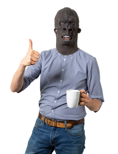 Goril maskeli bir adam baş parmağını kaldırıyor ve elinde kahve fincanı tutuyor. İzole edilmiş beyaz arka plan. Orta boy..  - Fotoğraf, Görsel