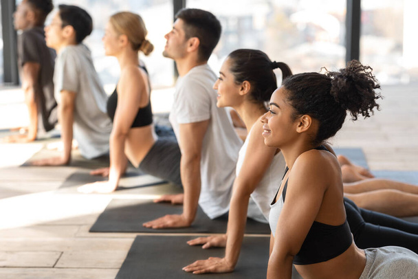 Різноманітні чоловіки та жінки практикують позу кобри під час уроку групової йоги
 - Фото, зображення