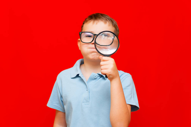Beautiful european young boy with eye glasses holding and looking through magnifying glass.He hold breath - Fotó, kép