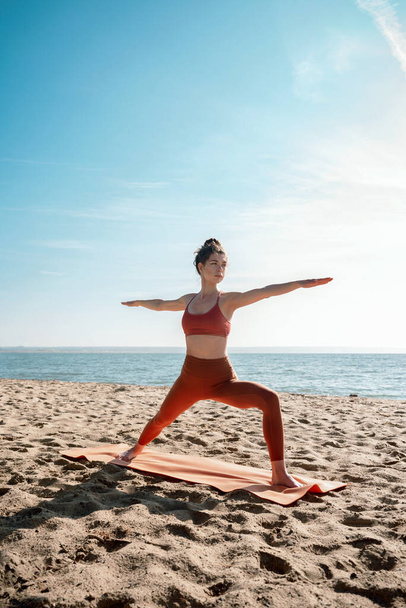 Young adult female practising yoga on a beach, Virabhadrasana II pose, selective focus - Photo, Image