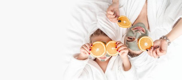 Уход за кожей, красота, спа. мать и дочь в белых халатах, нанося оранжевые части на глаза, в белом полотенце для ванны, позируя перед камерой дома, трогая лицо. - Фото, изображение
