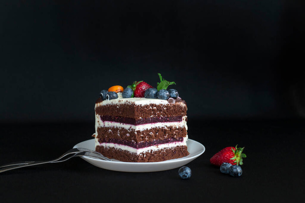 Warstwowe ciasto czekoladowe ozdobione kwiatami i jagodami na stole ogrodowym. - Zdjęcie, obraz
