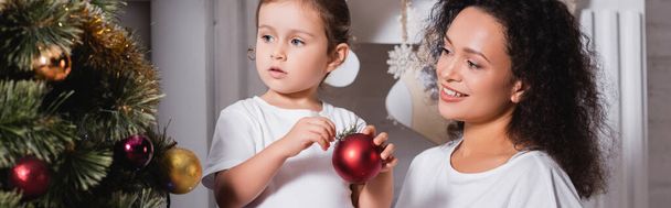 Panoramic shot of mother and daughter decorating christmas pine near fireplace - Fotografie, Obrázek