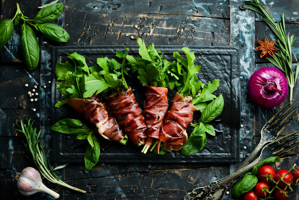 Prosciutto with arugula and balsamic sauce on a black stone plate. Antipasto. Top view. - Фото, зображення