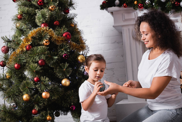 Evde süslü çam ağacının yanında oturan anne ve kız Noel topları. - Fotoğraf, Görsel