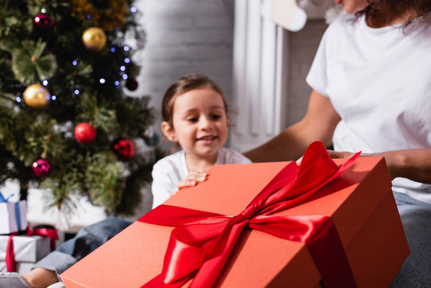 Selective focus of big gift box with red ribbon near mother and daughter  - Photo, Image