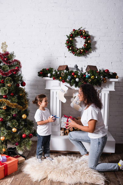 Side view of mother and daughter with gifts looking at each other at home - Foto, Imagen