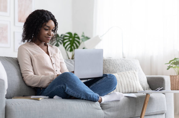 Éducation en ligne. Jeune femme noire étudiant avec ordinateur portable sur le canapé à la maison - Photo, image
