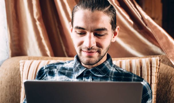 Egy jóképű fiatal szabadúszó kék ingben egy ezüst laptopon dolgozik otthon. Távmunka a karantén ideje alatt. - Fotó, kép