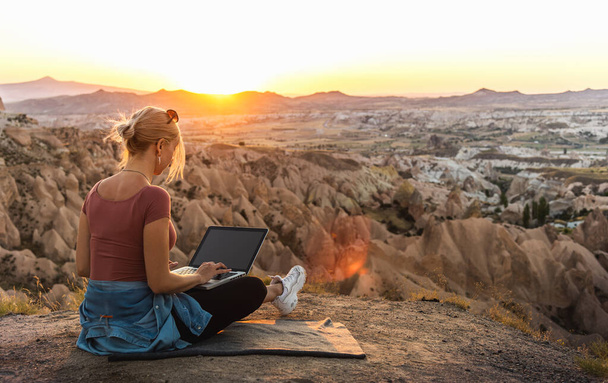 Young girl working at laptop at sunset on top of mountain with beautiful view at valley - Fotoğraf, Görsel