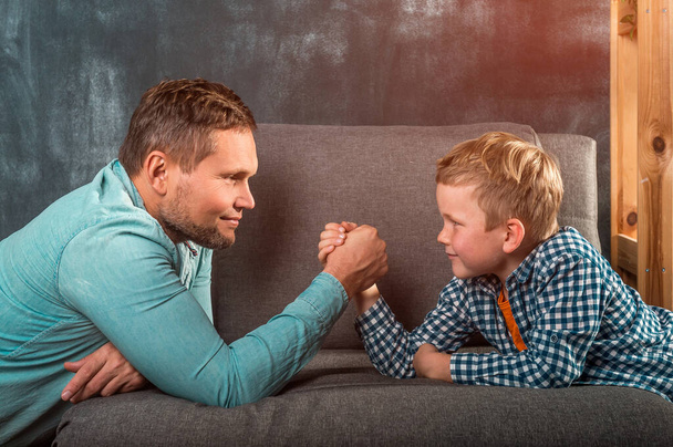 Father and son arm wrestling while having fun time together at home. Happy family - father and child playing. - Photo, Image