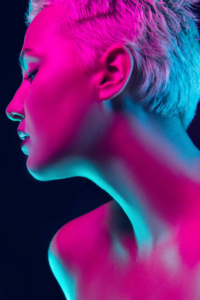 Portrait of female fashion model in neon light on dark studio background. - Фото, изображение