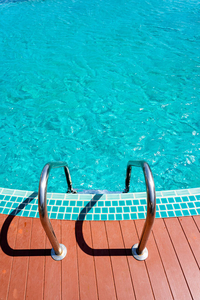 Empty turquoise swimming pool with steel ladder and wooden plank floor. - Photo, Image
