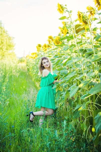blond european girl in a green dress  on nature with sunflowers - Фото, изображение
