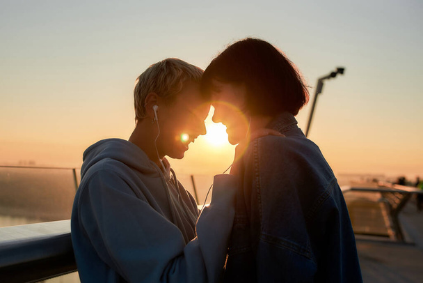 Young lesbian silhouetted couple, two happy women having romantic moment while listening to music sharing one same earphones - Φωτογραφία, εικόνα