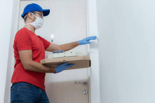 Доставщик в защитной маске держит коробку с пиццей у двери. - Фото, изображение