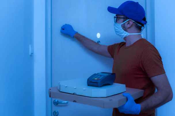 Zusteller mit Schutzmaske hält Pizzaschachtel vor der Tür. - Foto, Bild