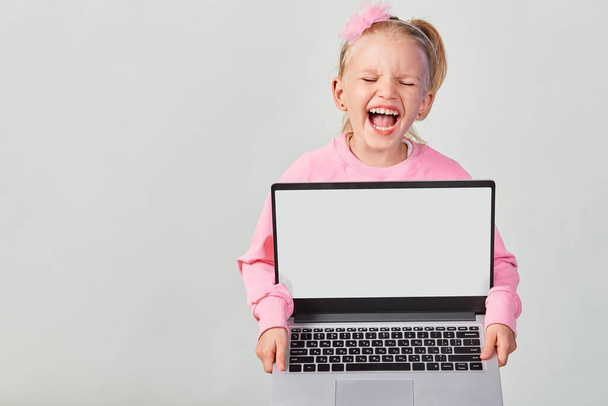 Closeup portrait of ?ute girl 4-5 year old in pink showing laptop screen with mock up on gray background - Photo, Image