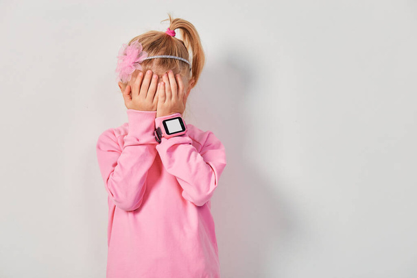 4-5 yaşlarında sevimli beyaz bir kız. Bileğinde akıllı bir saat var. Çocuklar için teknoloji, gri stüdyo geçmişine karşı - Fotoğraf, Görsel