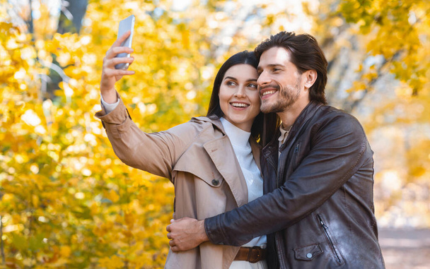Fröhlich umarmtes junges Paar macht Selfie im Freien - Foto, Bild