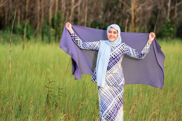 Porträt der glücklichen schönen jungen Model in modischen Hijab-Stil posiert im grünen Bereich, während sie Stoff hält. Stilvolles muslimisches Hijab-Mode-Lifestyle-Porträtkonzept. - Foto, Bild
