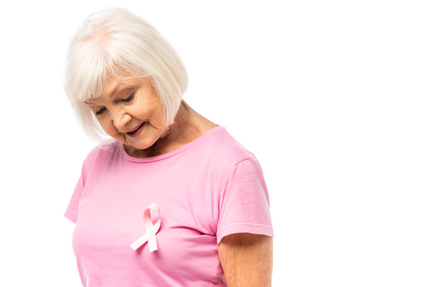 Elderly woman looking at pink ribbon of breast cancer awareness on t-shirt isolated on white - Фото, изображение