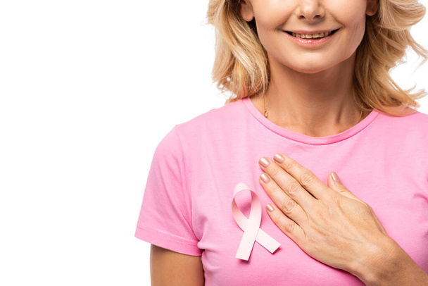 Προβολή της ξανθιάς γυναίκας με το χέρι στο στήθος με κορδέλα ευαισθητοποίησης του καρκίνου του μαστού σε t-shirt που απομονώνονται σε λευκό - Φωτογραφία, εικόνα