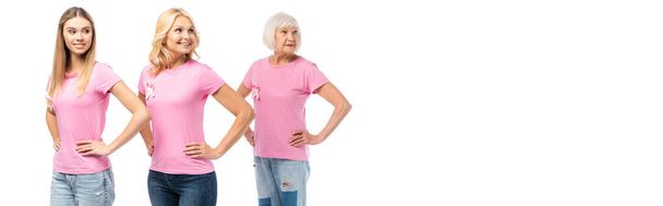 Panoramic crop of women with pink ribbons of breast cancer awareness and hands on hips looking away isolated on white - Photo, Image