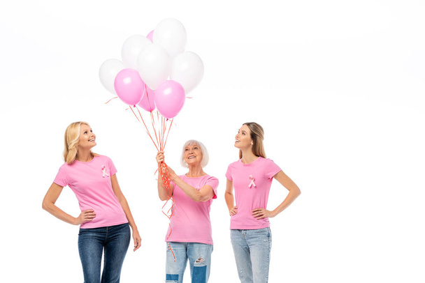Frauen mit Brustkrebs-Bewusstseinsbändern auf T-Shirts, die Luftballons auf weißem Grund betrachten - Foto, Bild