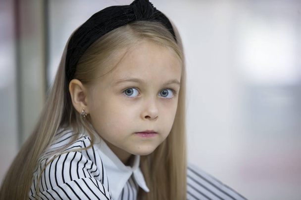 Το πρόσωπο ενός όμορφου ξανθού κοριτσιού με μπλε μάτια. Ένα παιδί της στοιχειώδους ηλικίας. - Φωτογραφία, εικόνα