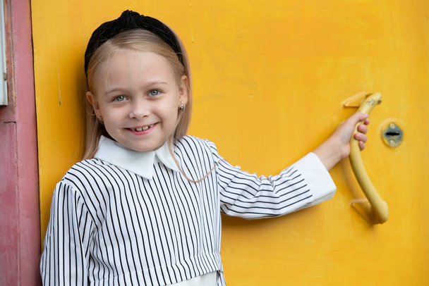 Счастливая маленькая девочка улыбается в камеру напротив желтой стены. - Фото, изображение