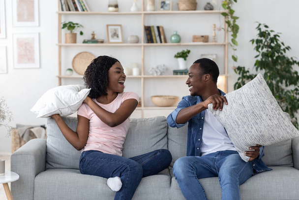 Happy loving black couple fighting with pillows in living room - Foto, Imagem