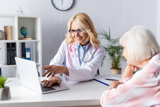 Arts wijzend met de hand en patiënt op zoek naar laptop op tafel in de kliniek - Foto, afbeelding
