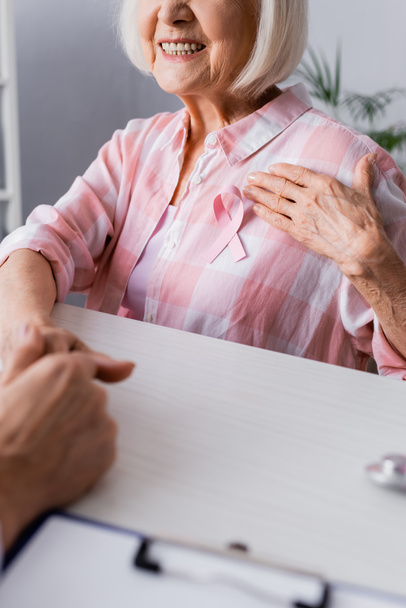 Cropped view of elderly woman with hand on breast near pink ribbon  - Foto, Bild