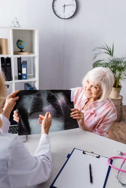 Orvos és idős nő tartja és nézi a mellkasröntgen a munkahelyen - Fotó, kép