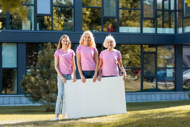 Τρεις γυναίκες σε ροζ μπλουζάκια με άδειο πίνακα, έννοια του καρκίνου του μαστού - Φωτογραφία, εικόνα