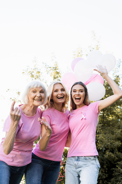 Emocionado tres mujeres con cintas rosas sosteniendo globos al aire libre - Foto, imagen