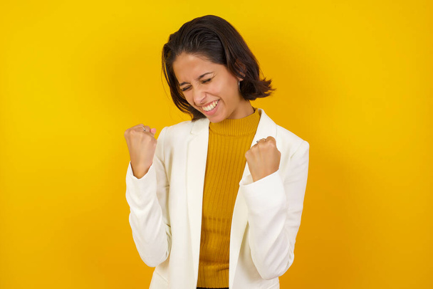 Caucasian brunette woman rejoicing her success and victory clenching her fists with joy. Lucky woman with hair bun being happy to achieve her aim and goals. Positive emotions, feelings. - Photo, Image