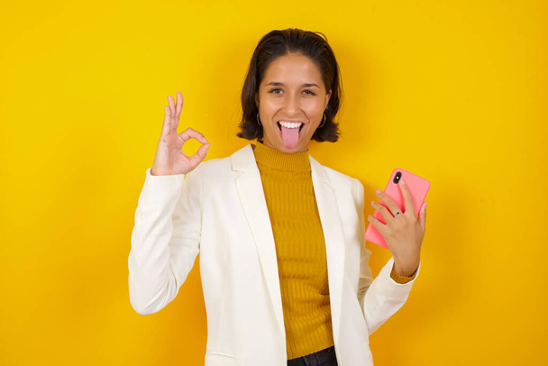 Porträt eines ziemlich glücklichen kaukasischen Mädchens, das ein Selfie auf gelbem Hintergrund macht - Foto, Bild