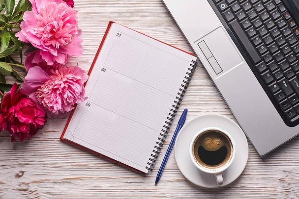 フラットレイアウトの女性のオフィスデスク。ノートパソコン付きの女性ワークスペース、ピンクの牡丹の花束と白い背景のコーヒー。トップ表示女性の背景. - 写真・画像