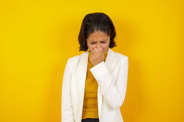 Young beautiful woman standing against yellow background, holding her nose because of a bad smell - Photo, Image