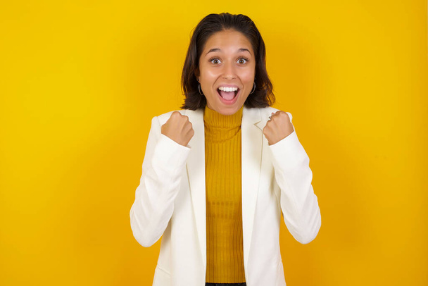Caucasian young woman rejoicing her success and victory clenching her fists with joy. Lucky woman with hat being happy to achieve her aim and goals. Positive emotions, feelings. - Photo, Image