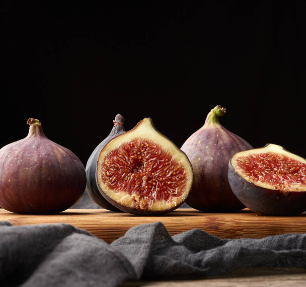 ripe whole and halved purple figs on a black napkin, low key, close up - Foto, afbeelding