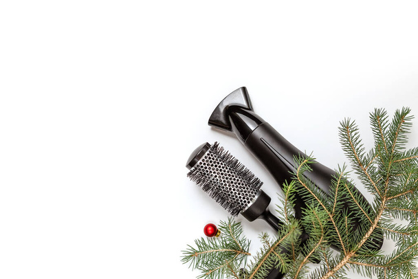 Christmas composition. Hairdressing tools and a spruce branch on a white background, hair dryer, comb. Template for a postcard or information about a hair salon. Flat lay, copy space - Photo, Image